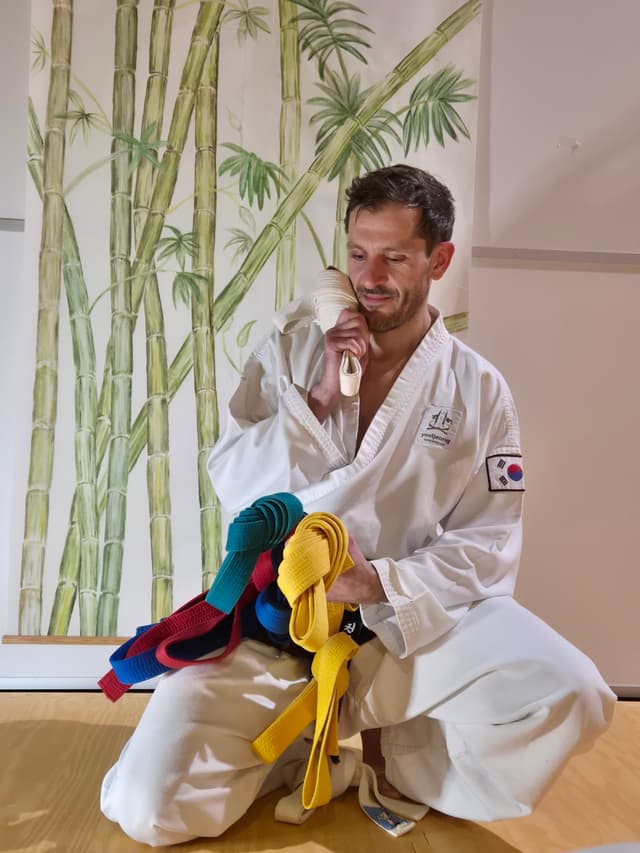 Nachdenklicher Kampfsport-Schulleiter steht vor ungeordneten bunten Gürteln – Symbol für den Organisationsaufwand bei der Gründung einer Kampfsportschule.